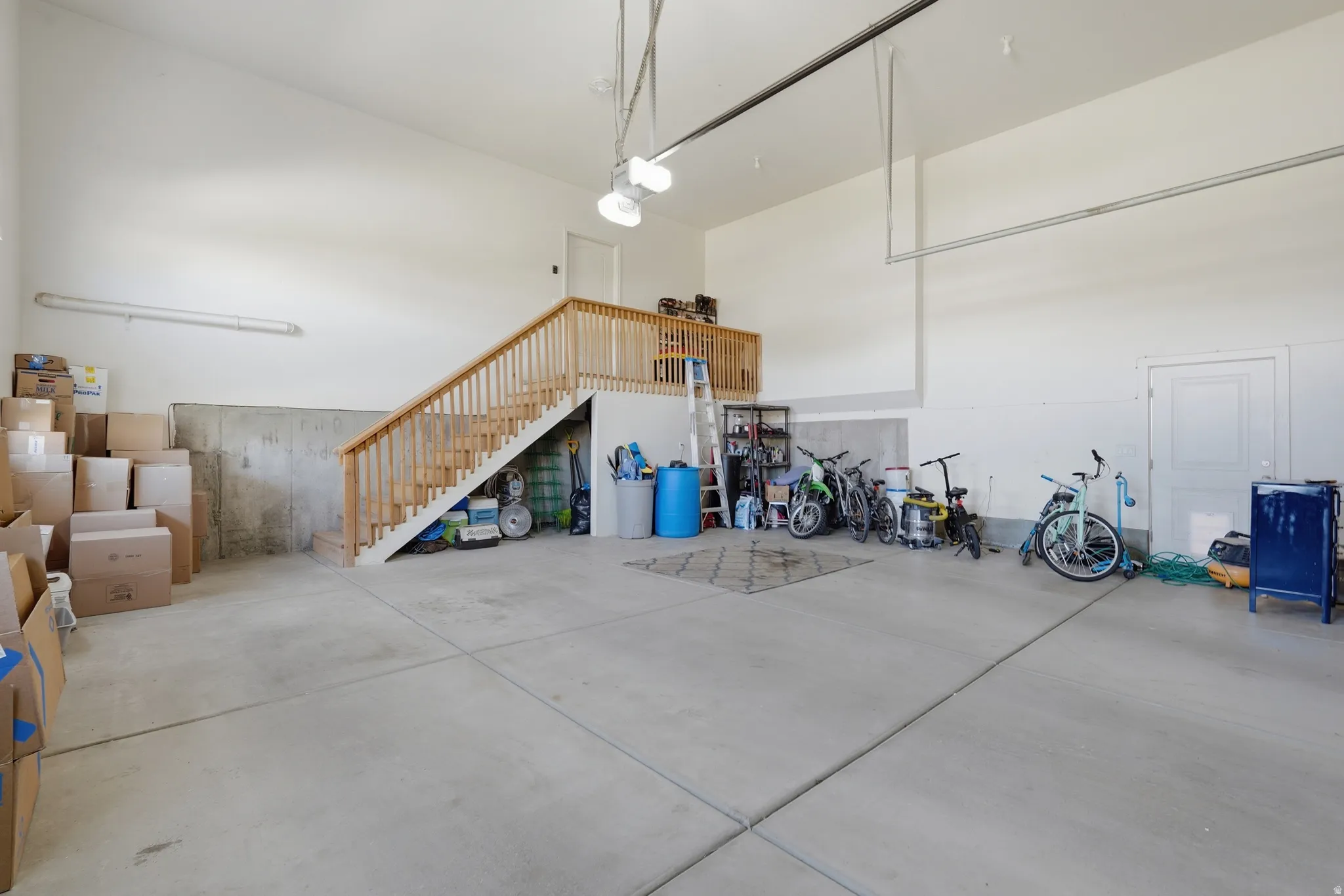 Spacious garage featuring a concrete floor, high ceilings, a wooden staircase, and an upper-level landing