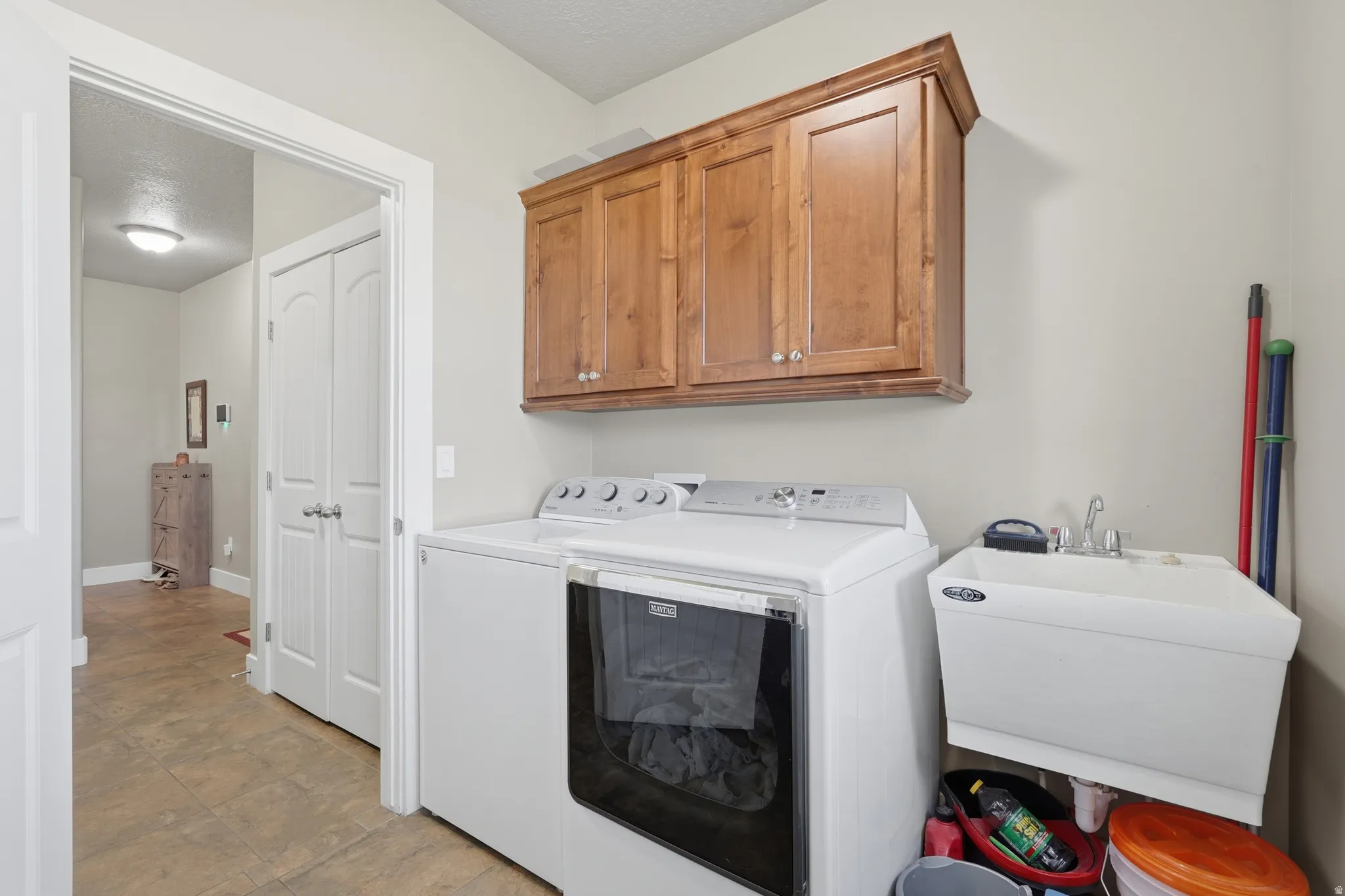 Dedicated laundry area featuring a utility sink, upper wood-finish cabinetry, and neutral wall paint