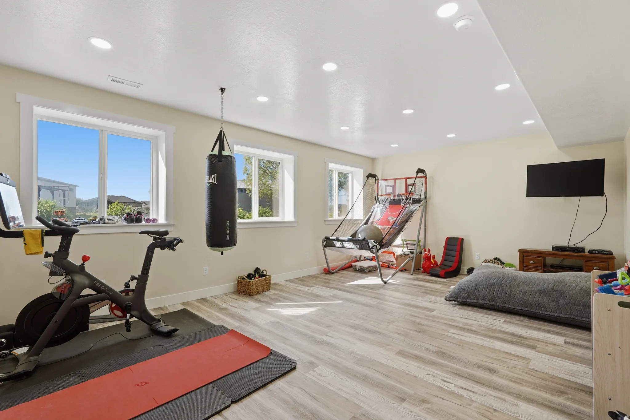 Spacious room featuring light-toned walls, recessed ceiling lighting, and wood-finish flooring