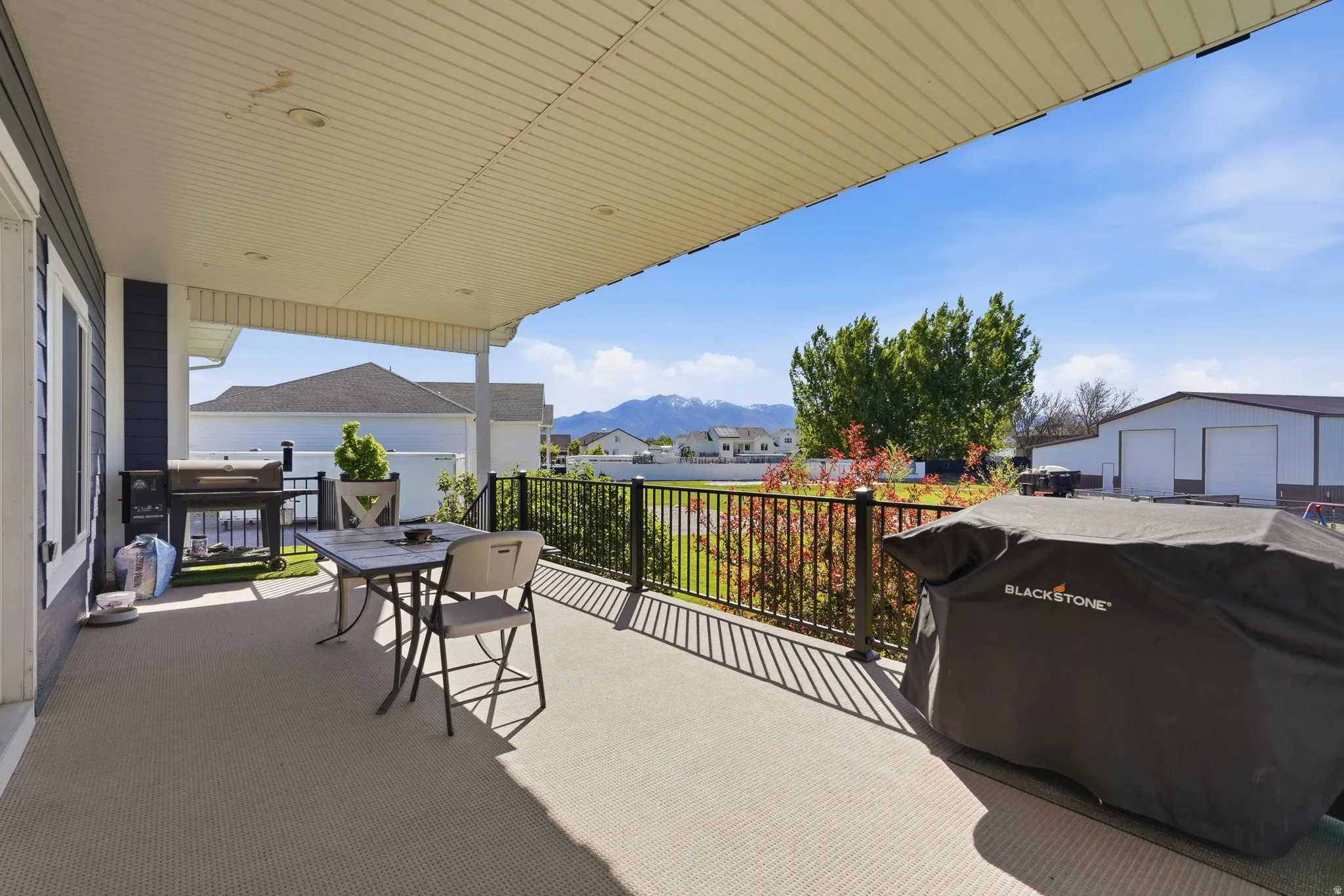 Covered outdoor patio with textured flooring, a dark gray siding exterior, and a black metal railing