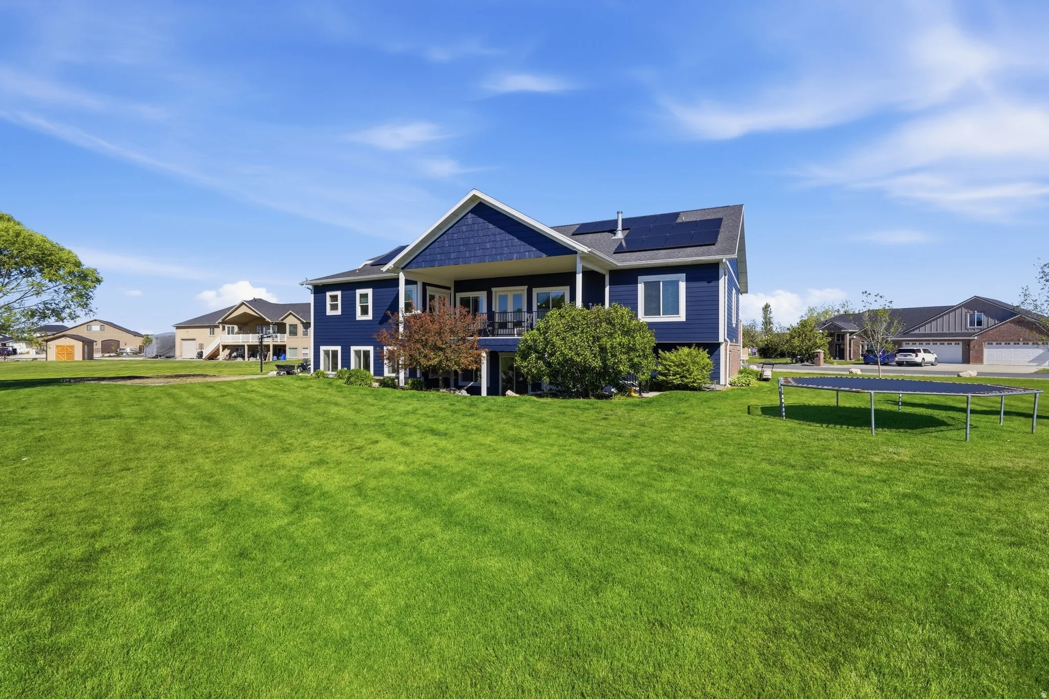 Expansive green lawn bordering a two-story home featuring dark blue siding, white trim, and solar panels on the roof