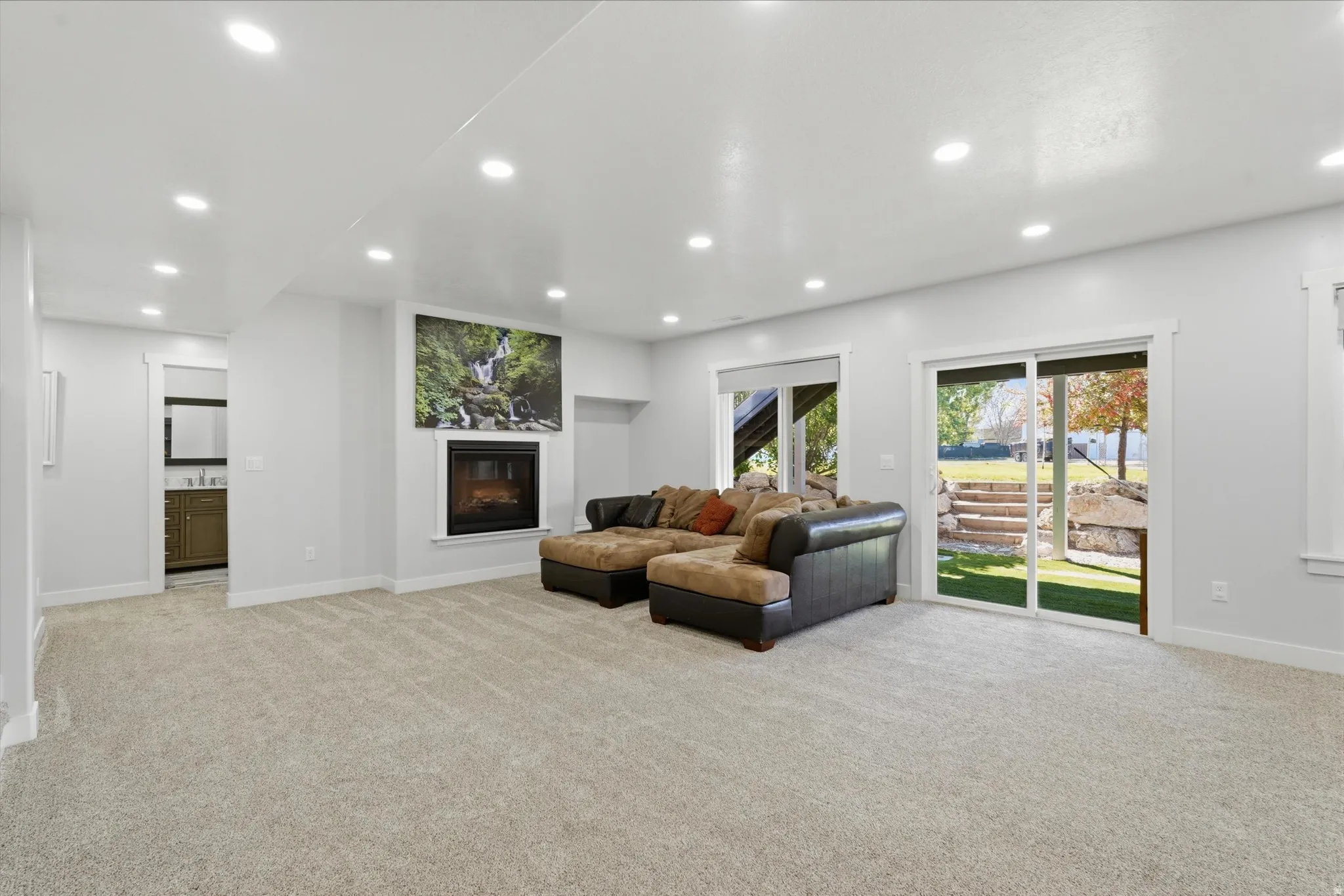 Spacious room featuring light-colored carpeting, recessed lighting, and a modern fireplace with a black surround