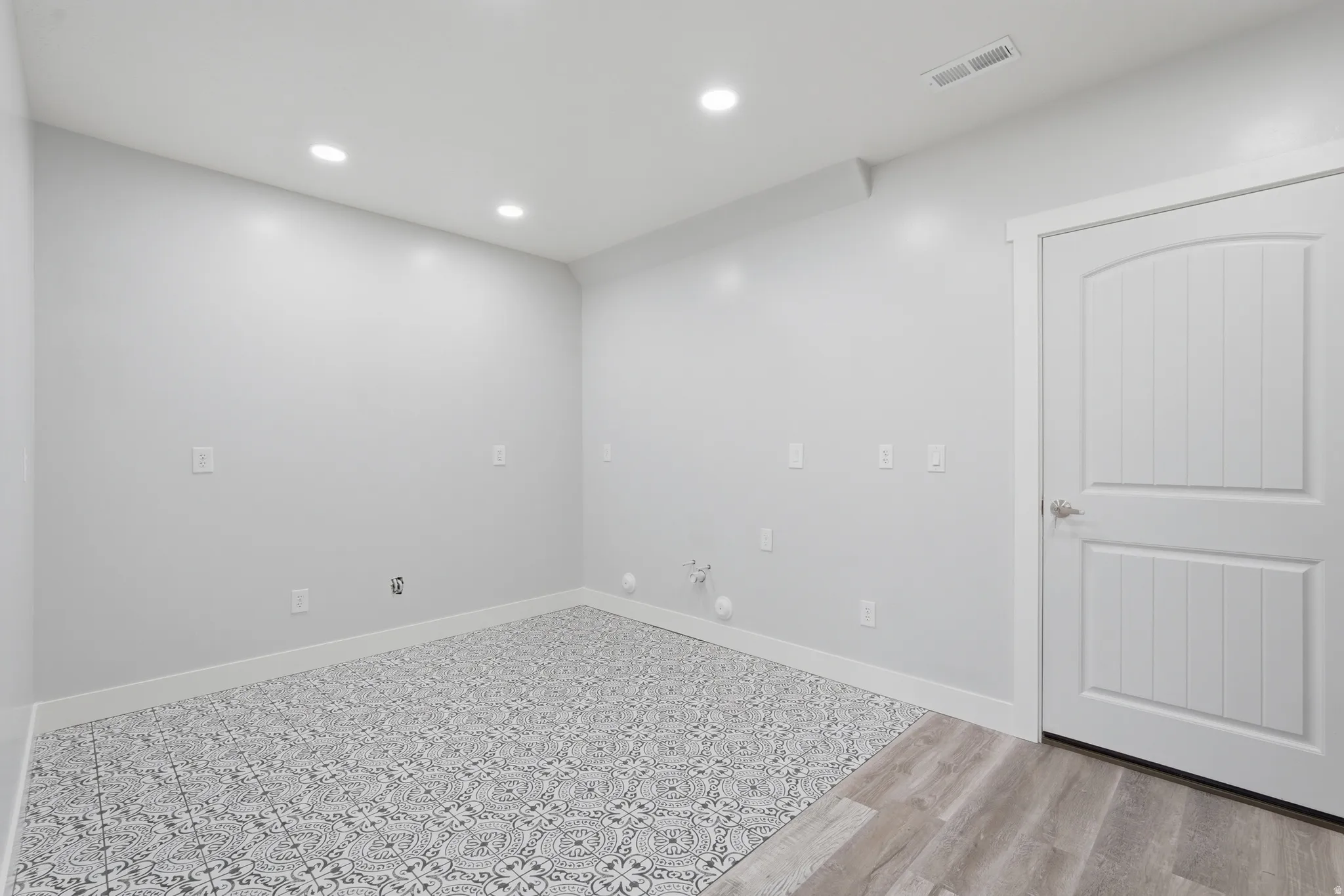 Room featuring recessed lighting, a patterned floor tile, wood-finish flooring, a white paneled door, and white baseboards