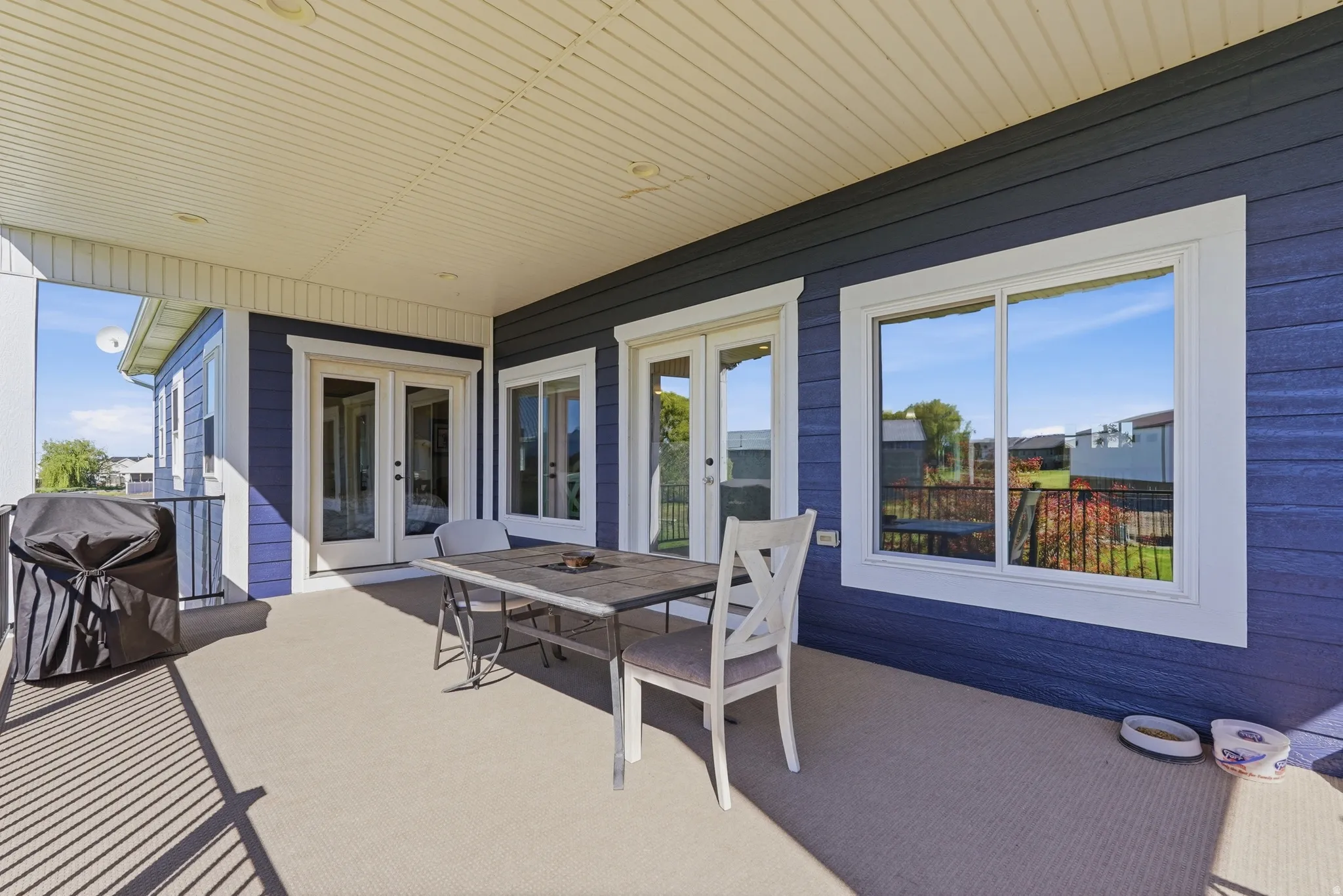 Covered patio featuring blue horizontal siding, white trim windows, double glass doors, a textured flooring surface, and a white beadboard ceiling with recessed lighting