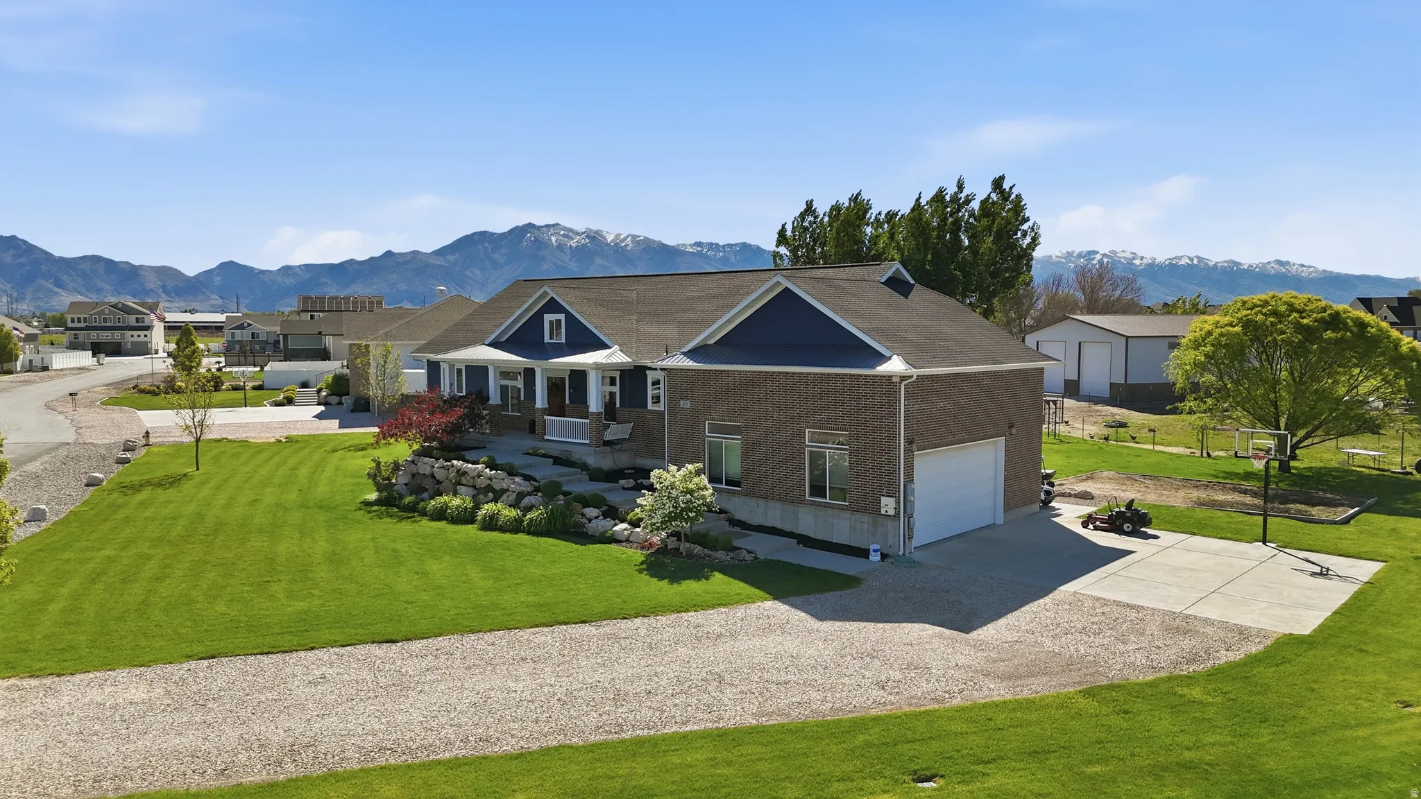 Brick and siding exterior with a covered porch, an attached garage, a gravel driveway, and a concrete pad