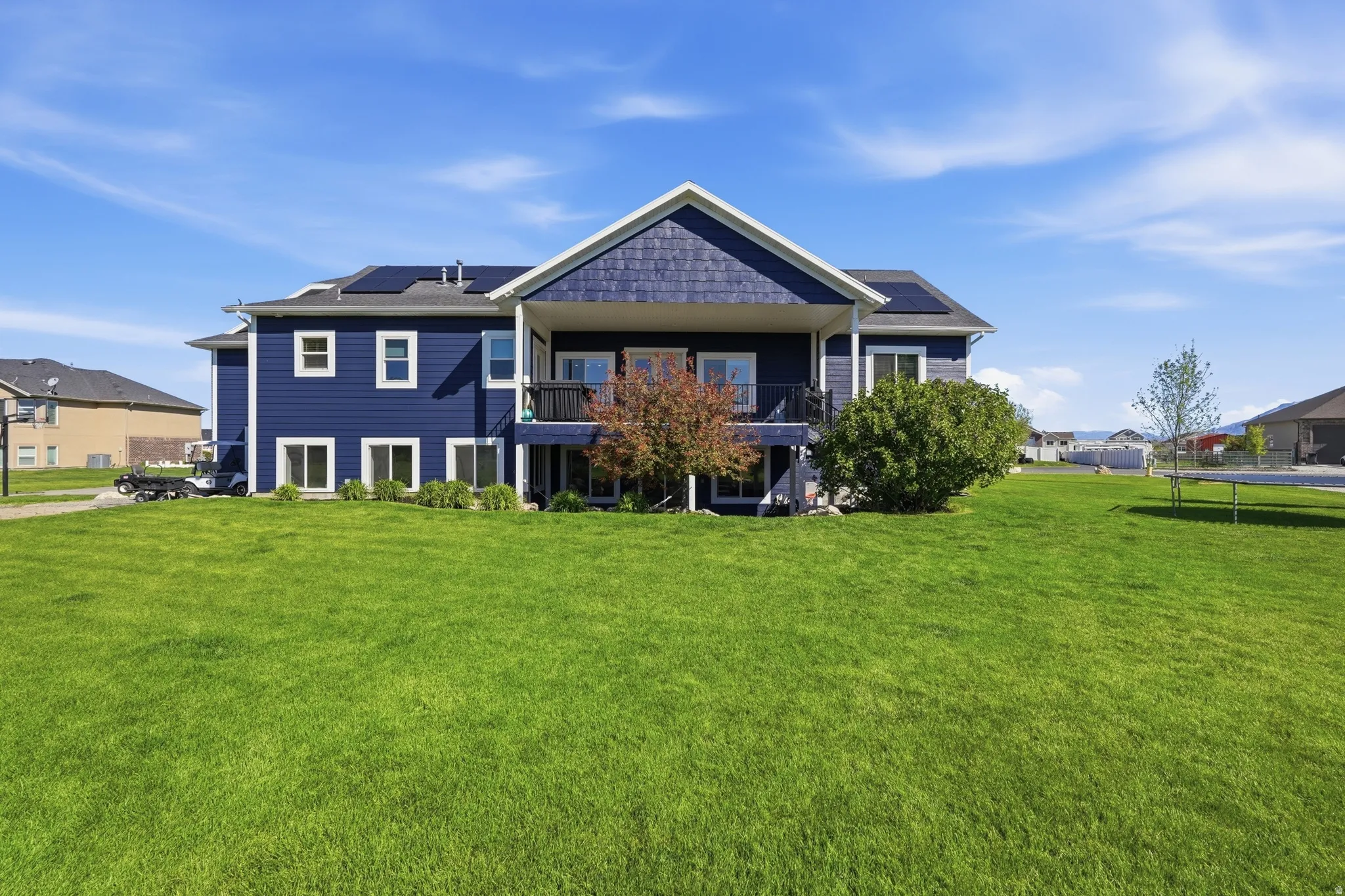 Expansive rear lawn featuring a two-story residence with dark blue siding and white window trim