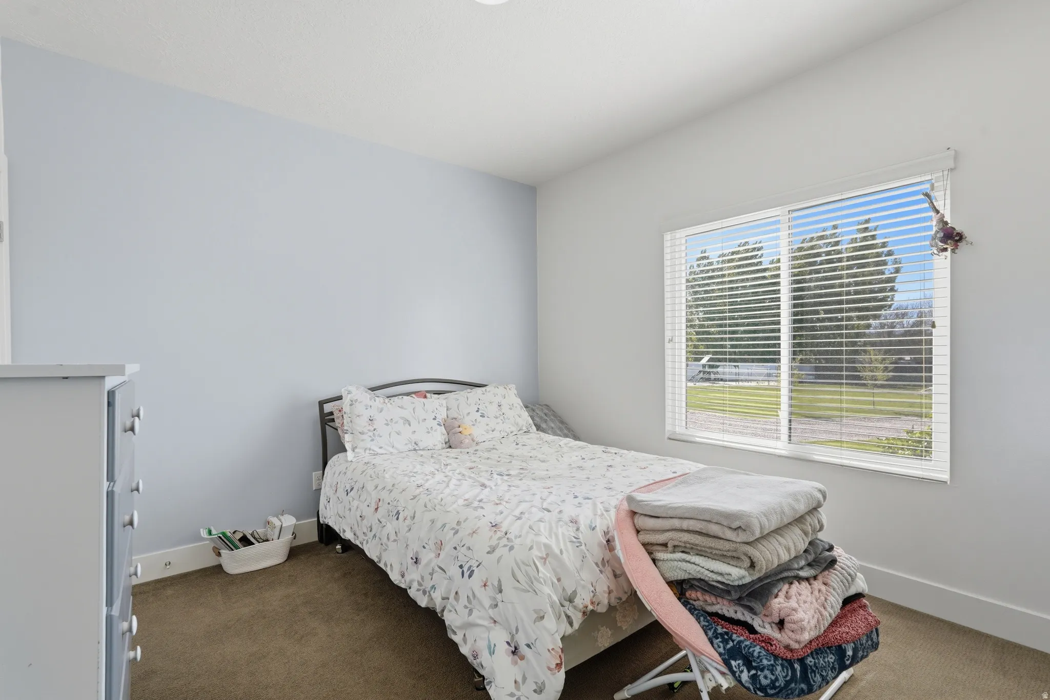 Bedroom featuring a large window with white blinds, light blue accent wall, and neutral carpeting