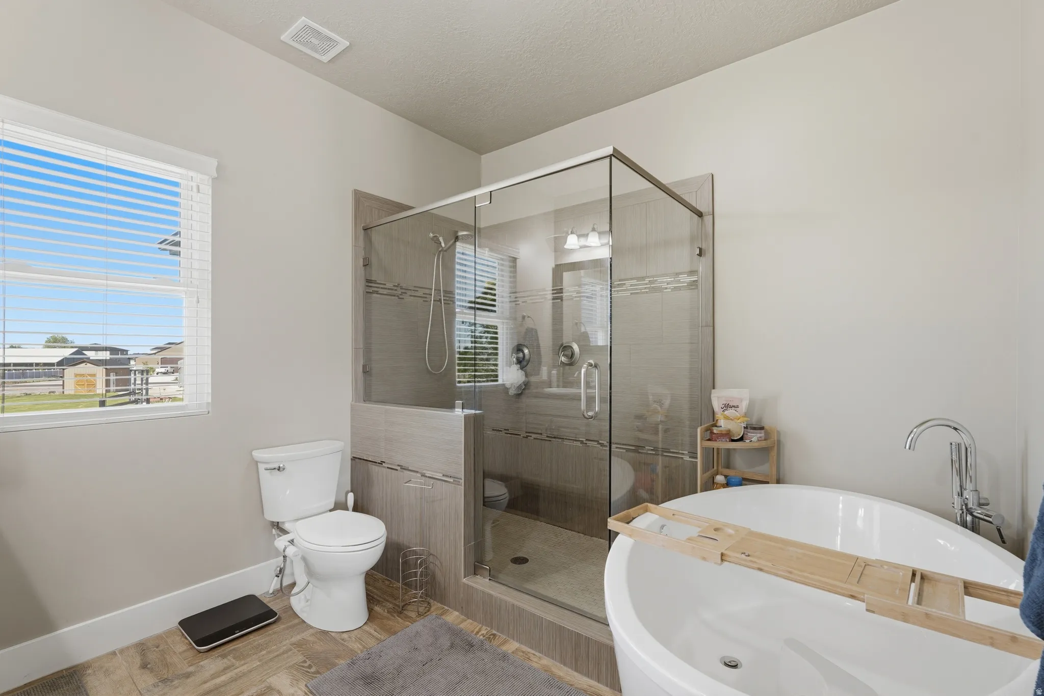 Freestanding soaking tub with chrome fixtures and wood-finish flooring
