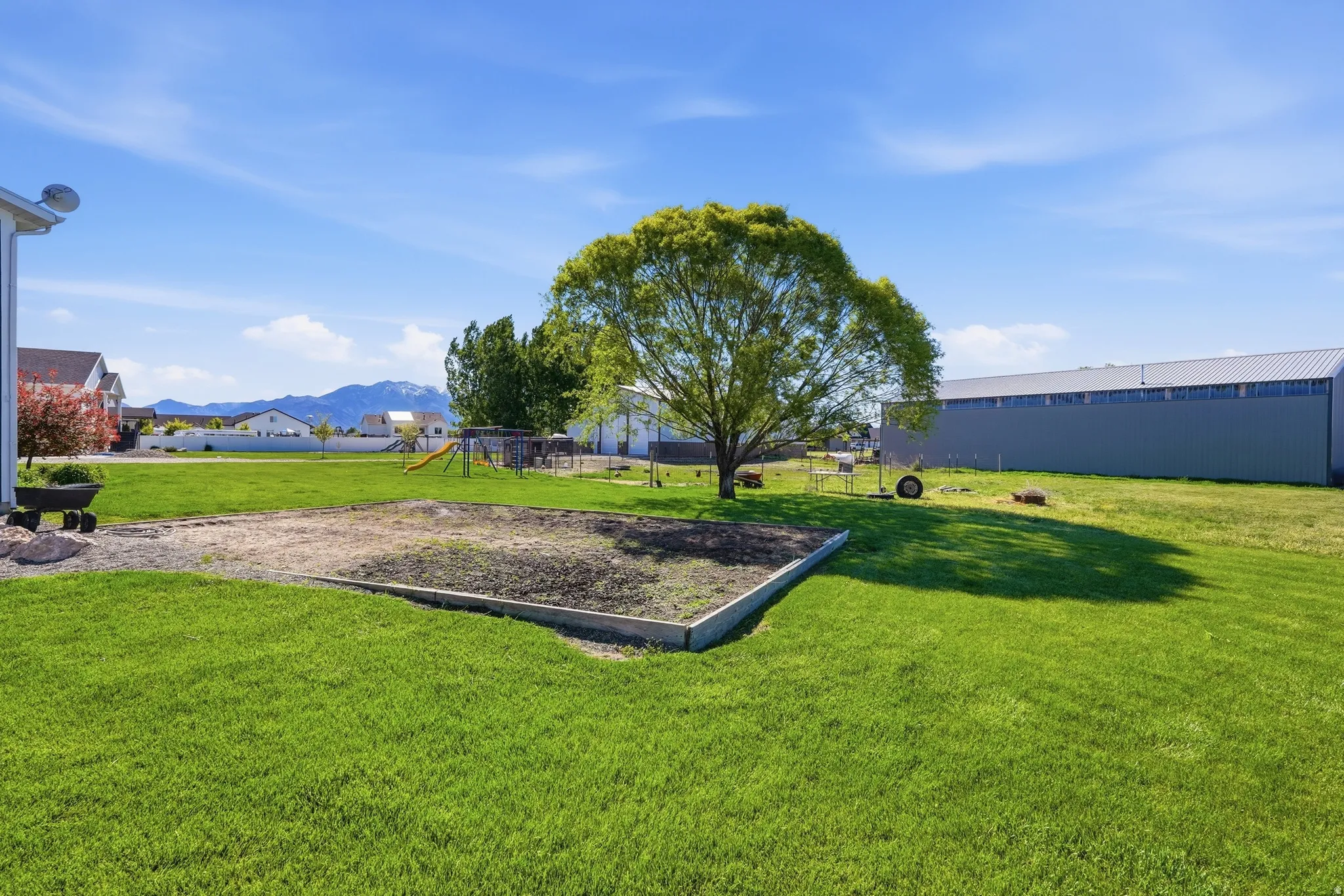 Expansive backyard with a large grassy area, a mature shade tree, a raised garden bed, and distant mountain scenery