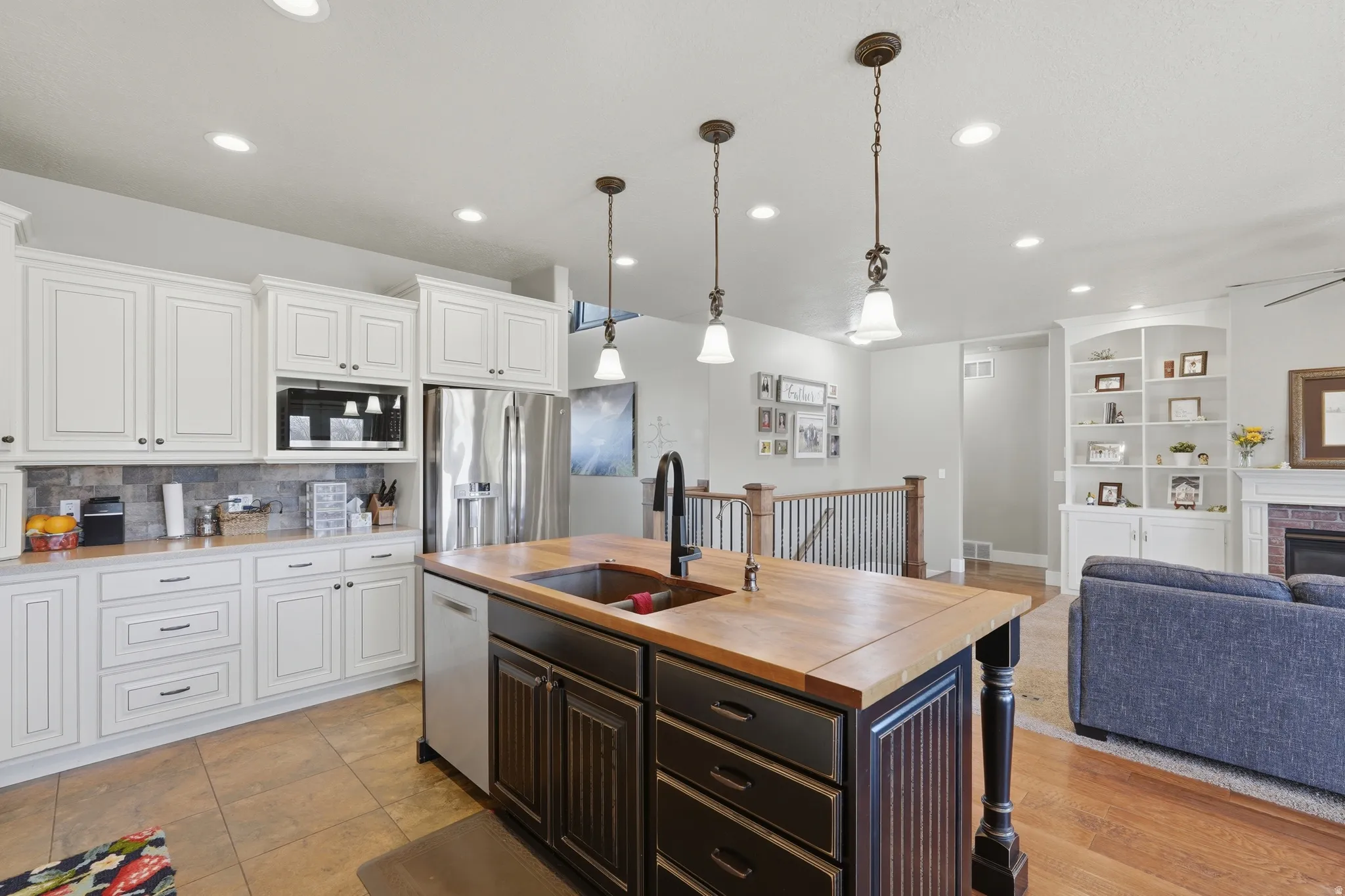 Open-concept kitchen featuring an island with a wood-finish countertop, white cabinetry with dark hardware, stainless steel appliances, and pendant lighting