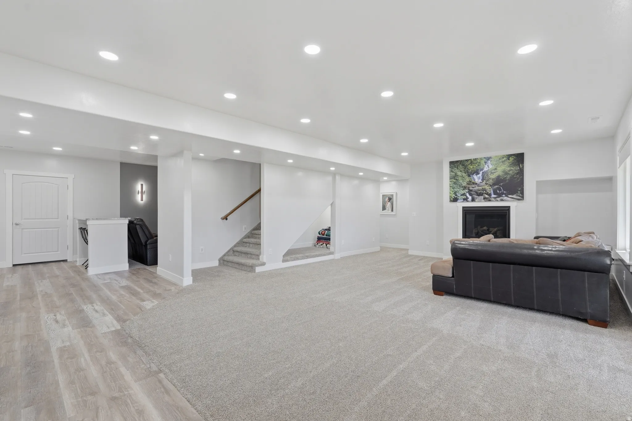 Spacious lower-level area featuring recessed lighting, a built-in fireplace, a dry bar, light wood-finish flooring, and soft carpeting