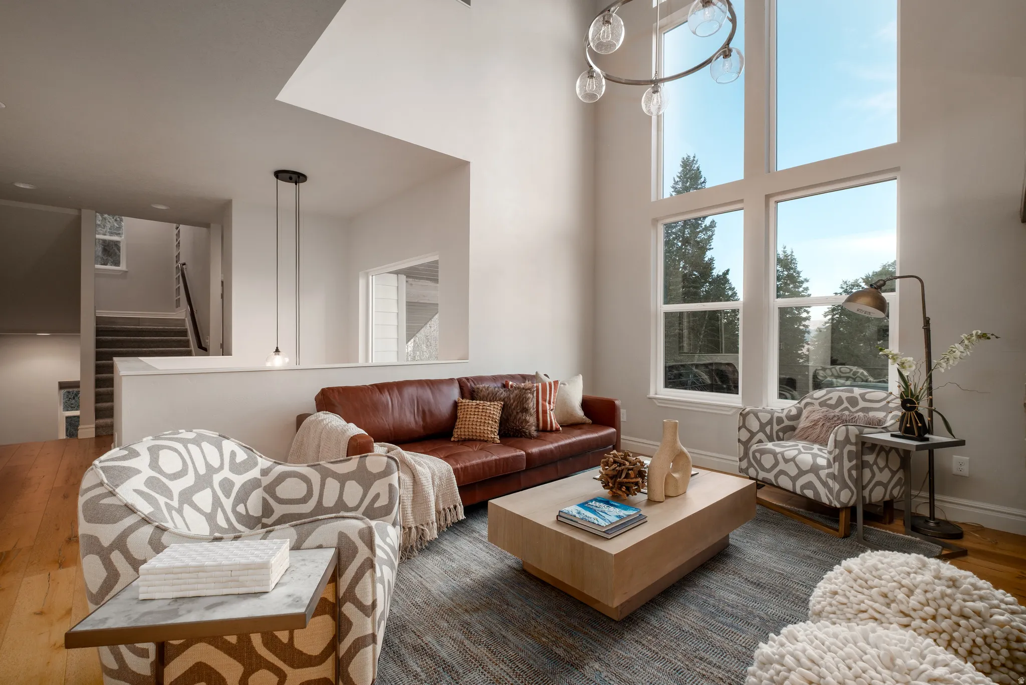 Vaulted ceiling living area featuring hardwood flooring, a large area rug, and significant natural light through multi-story windows