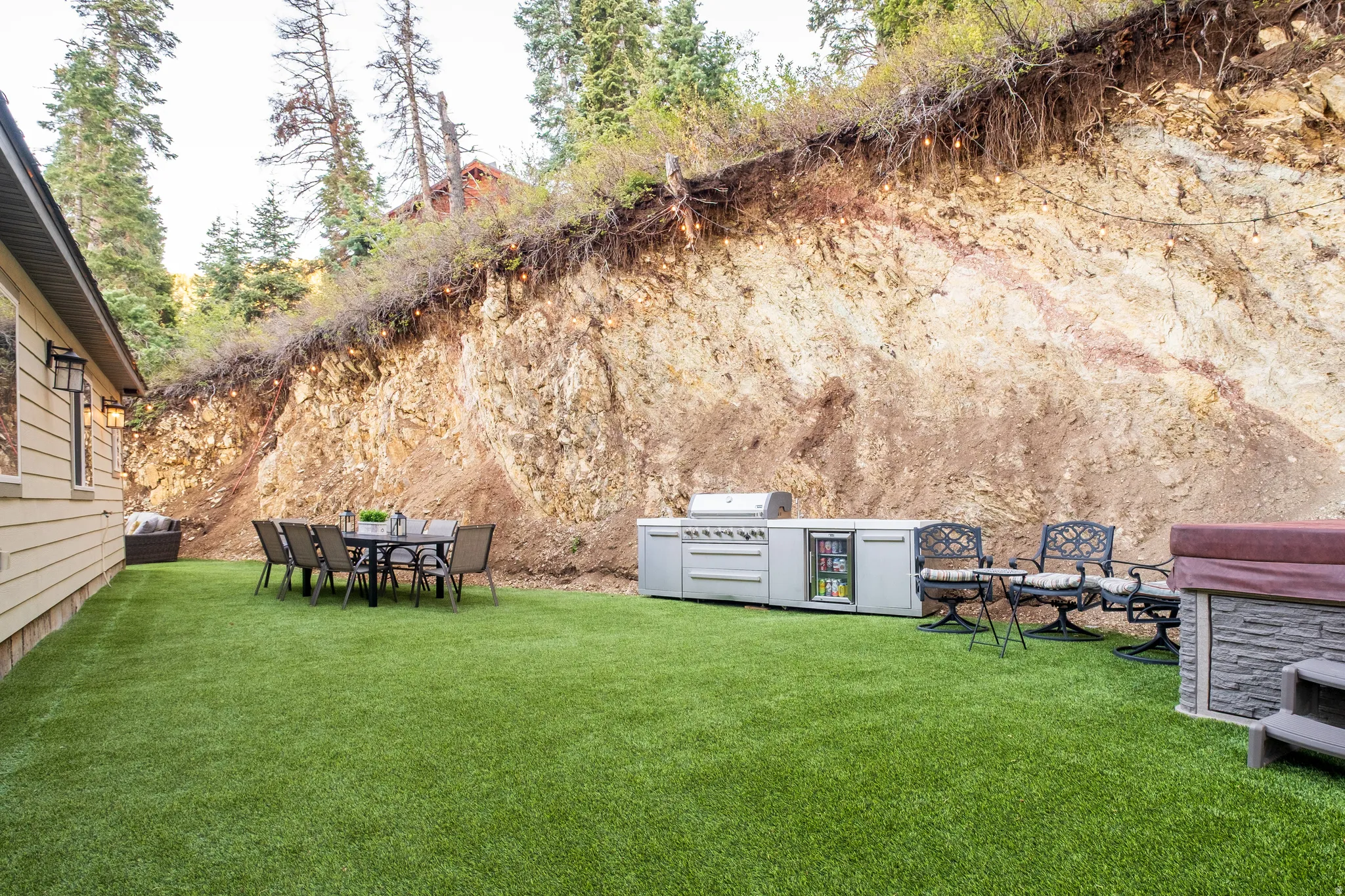 Expansive backyard featuring artificial turf, a built-in outdoor kitchen with grill and beverage refrigerator, and a hot tub with stone-look surround
