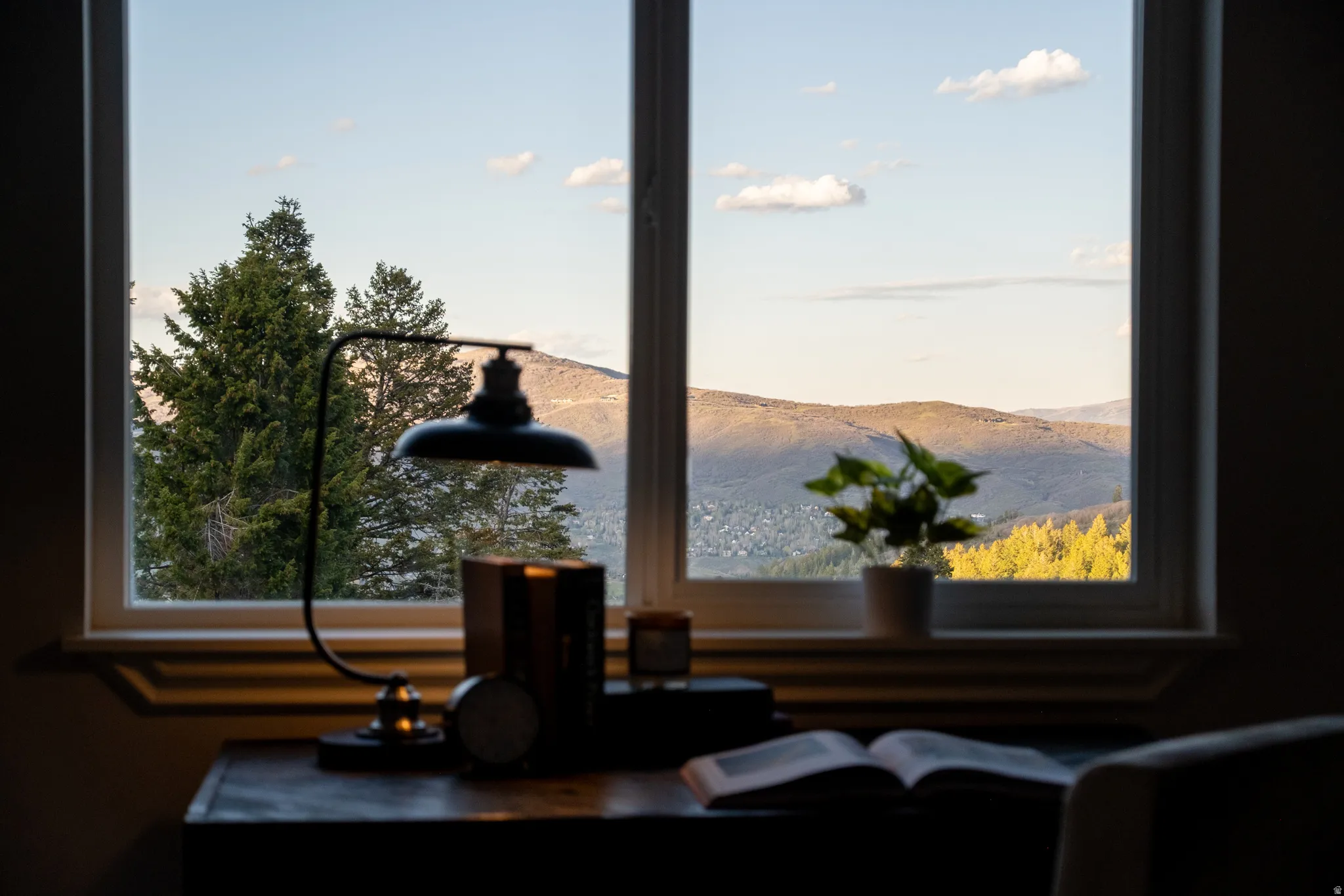 Window with white trim overlooking a mountainous landscape and distant evergreen trees