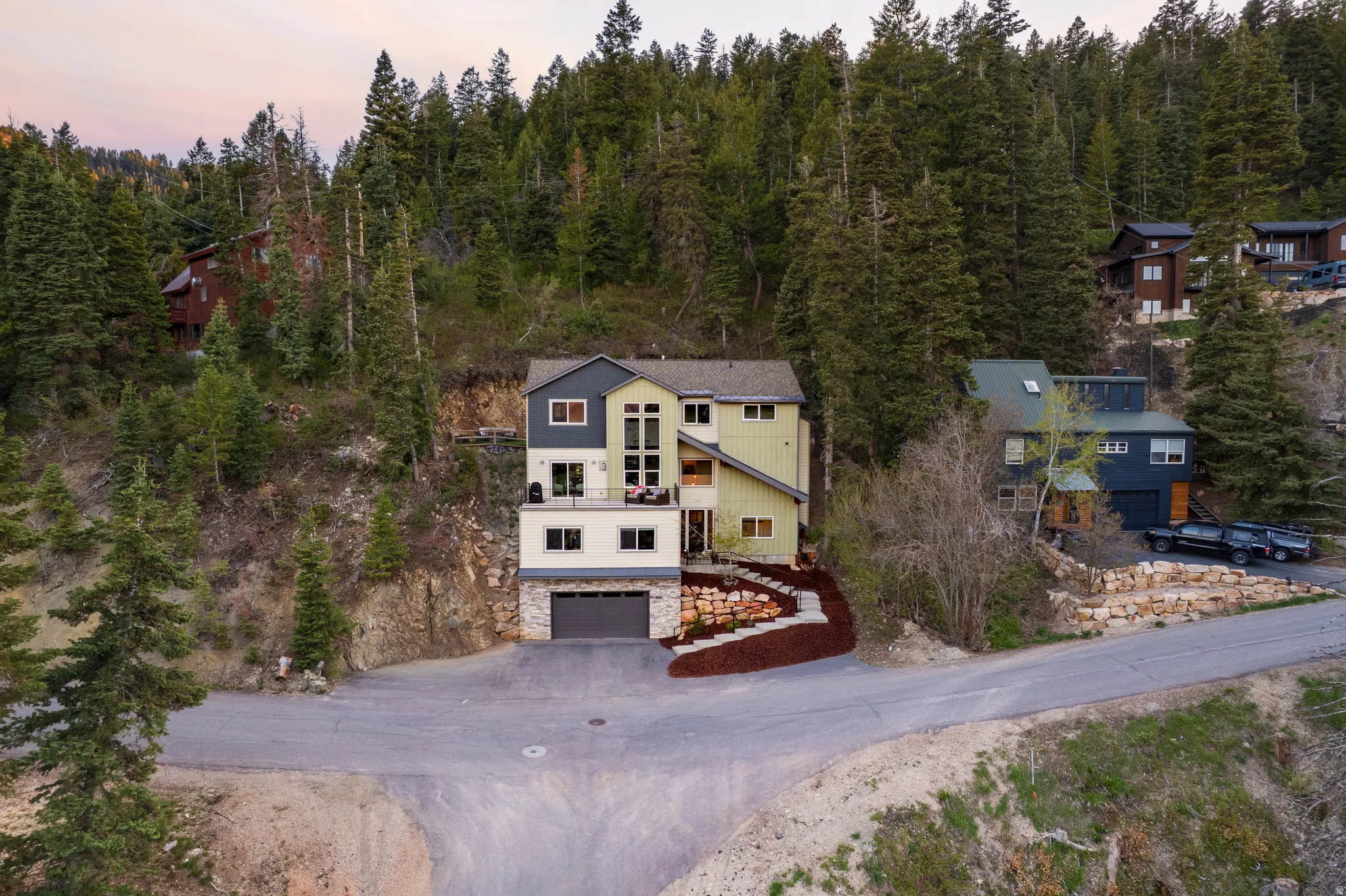Contemporary multi-story residence featuring a multi-tone exterior, a prominent garage, a second-story balcony, and a terraced rock garden leading to the entrance