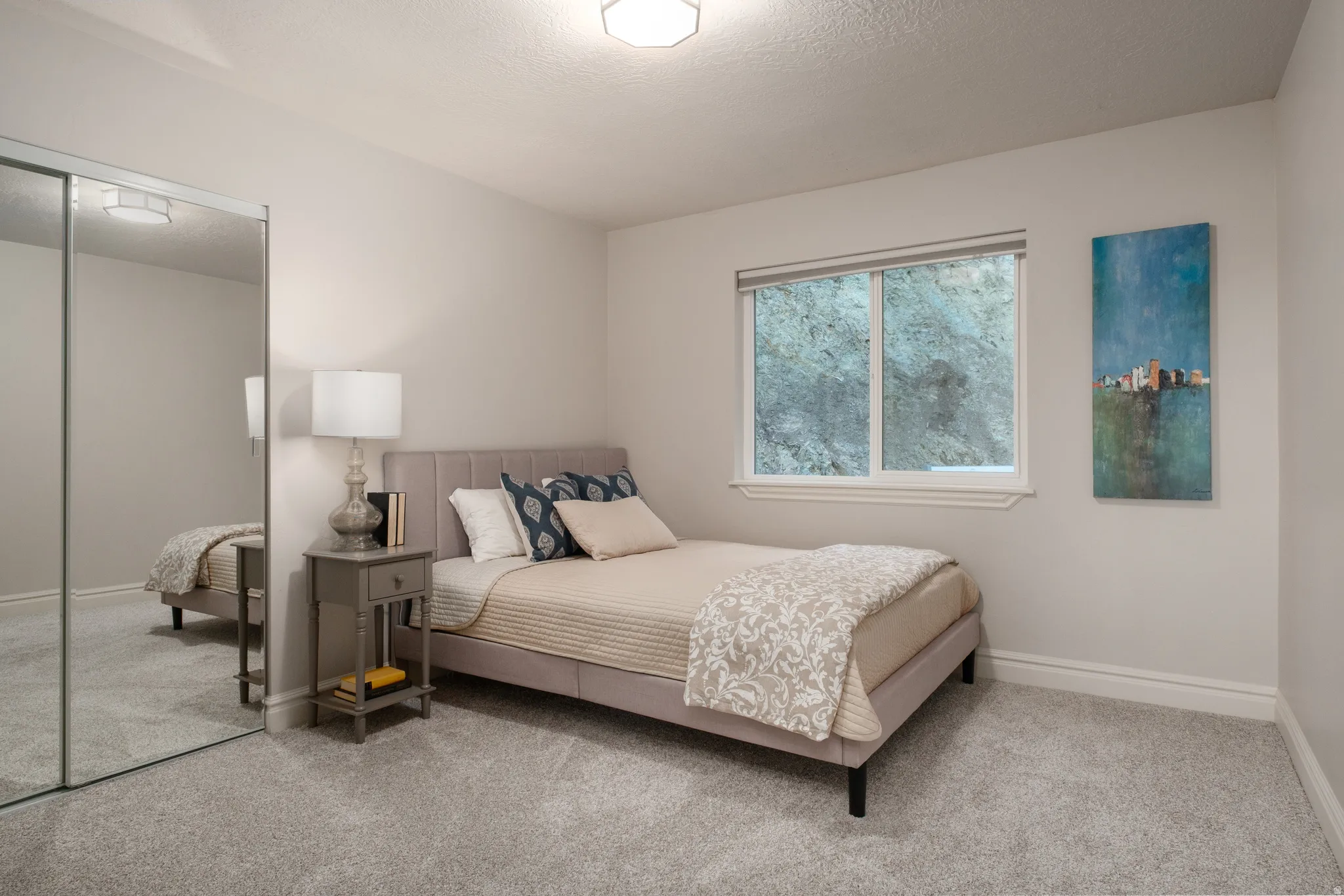 Bedroom featuring plush gray carpeting, a window with white trim, and mirrored sliding closet doors
