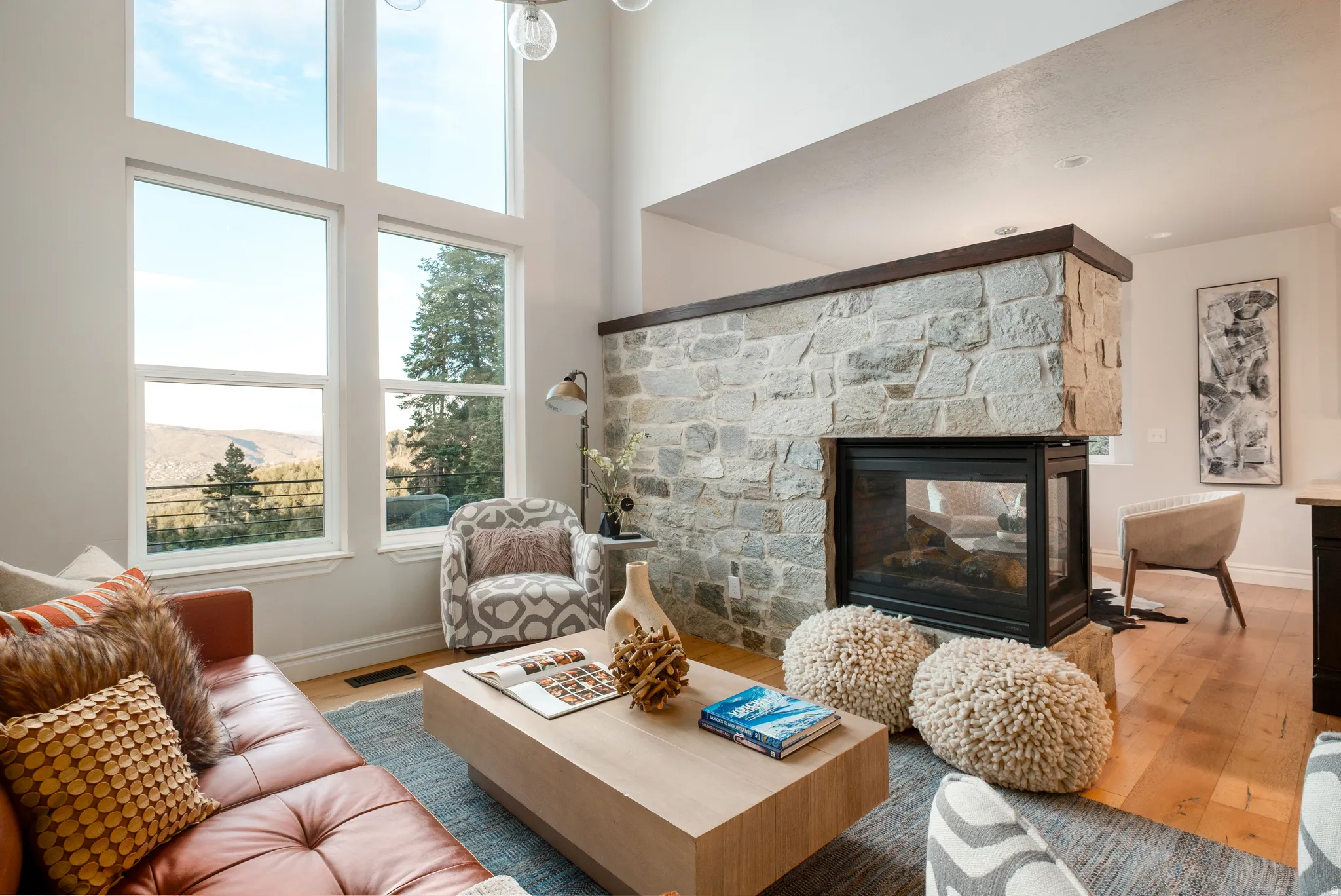 Living space featuring a stone-clad fireplace, high ceilings, large windows, wood-finish flooring, and recessed lighting