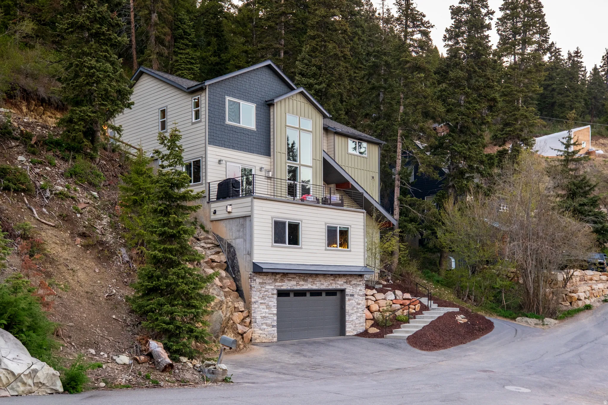 Multi-story contemporary residence featuring diverse siding materials, an integrated garage with a stone facade, and a balcony with a metal railing