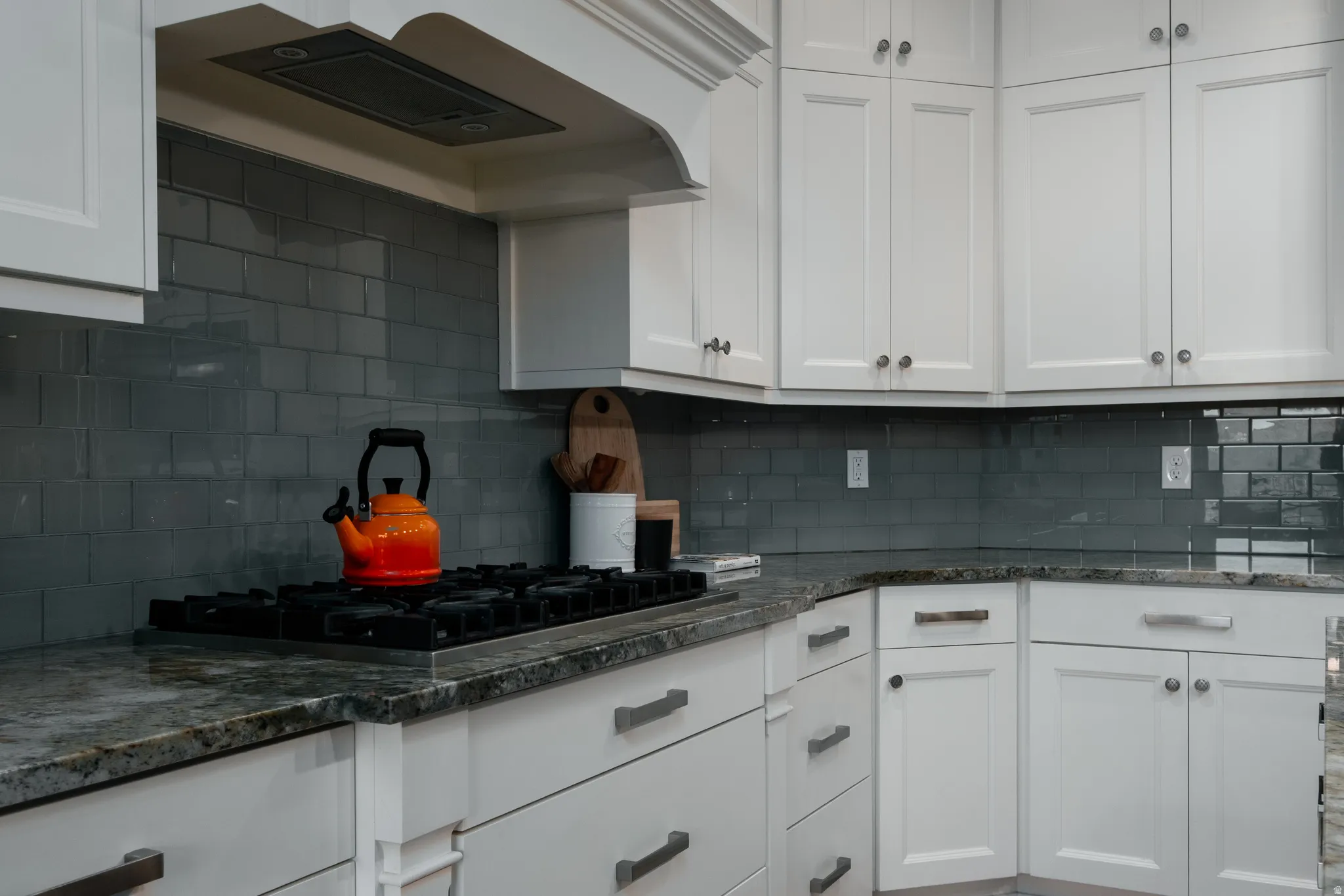 Kitchen featuring white cabinetry with silver-tone hardware, a built-in gas cooktop, natural stone countertops, and a subway tile backsplash