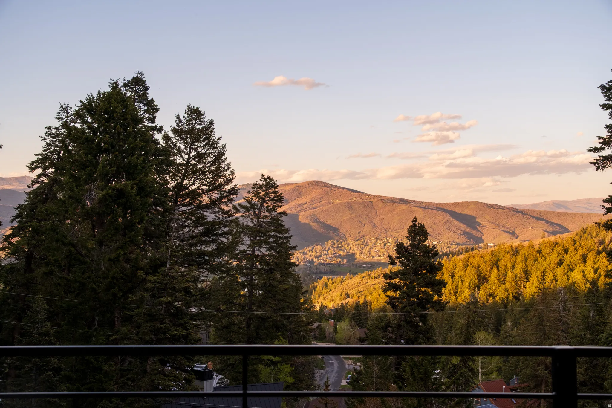 Expansive mountain landscape with a verdant forest, visible from a balcony featuring a black metal railing