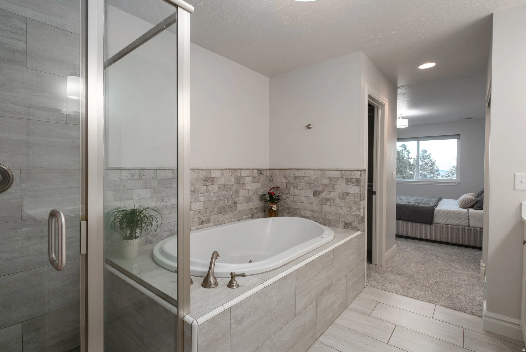 Bathroom featuring a built-in soaking tub with deck-mounted bronze fixtures, glass-enclosed shower with tile surround, and light gray tile flooring