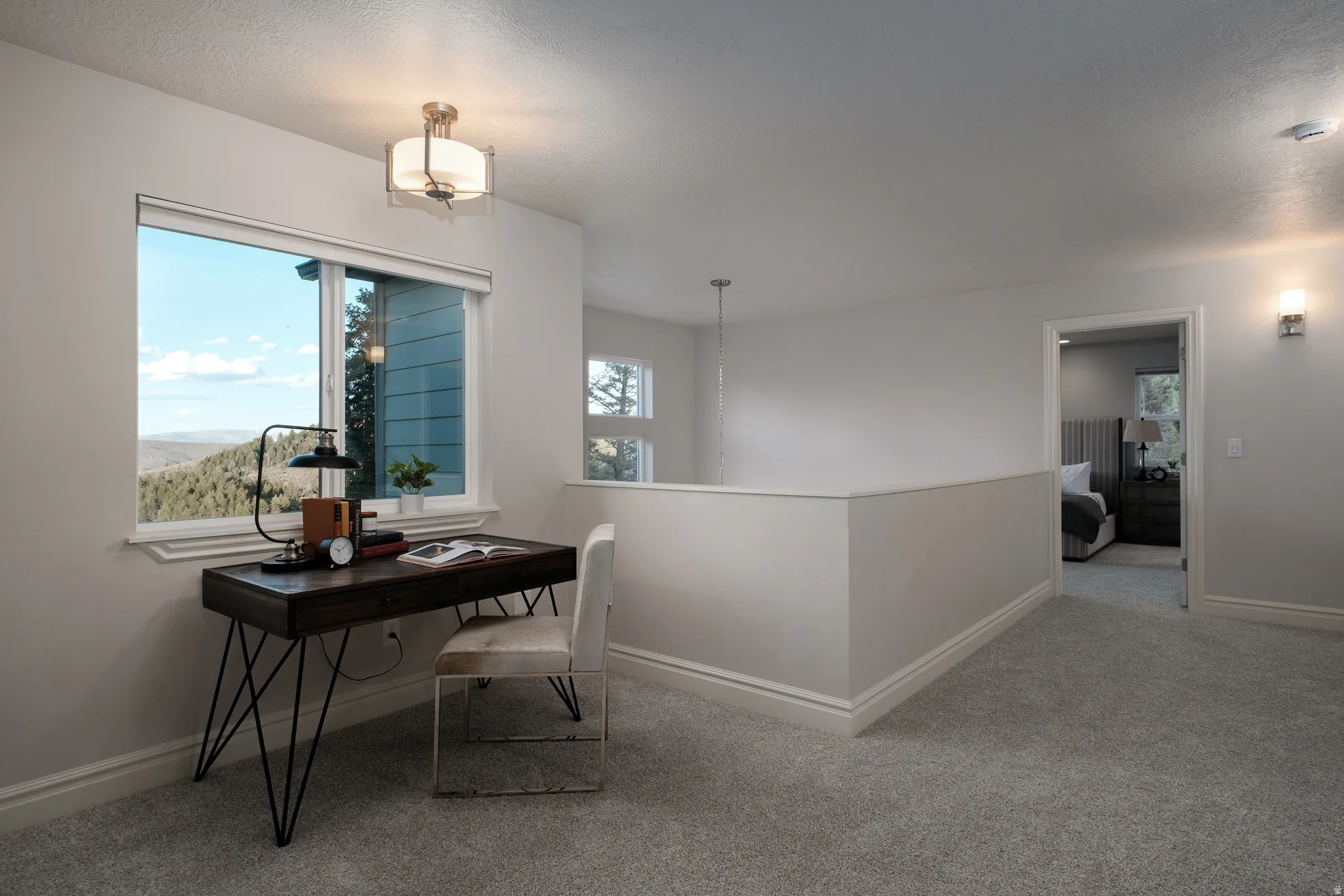 Upper-level landing featuring a window with a mountain backdrop, plush carpeting, a partial wall with a railing, and contemporary wall sconce lighting