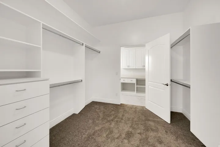Walk-in closet featuring white built-in cabinetry, shelving, and hanging rods