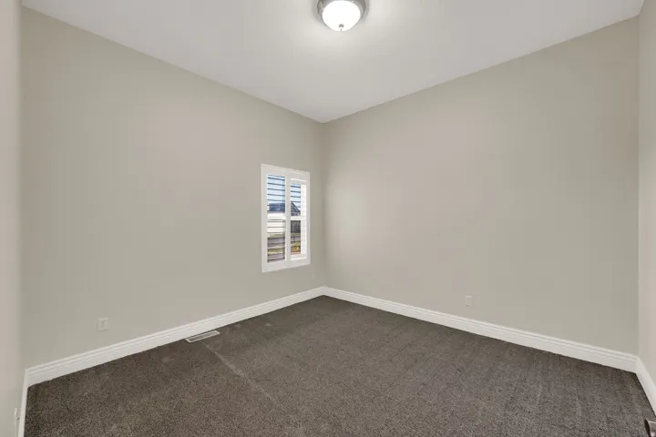 Neutral-toned room featuring a single window with white plantation shutters, neutral carpet flooring, and a flush-mount ceiling light fixture