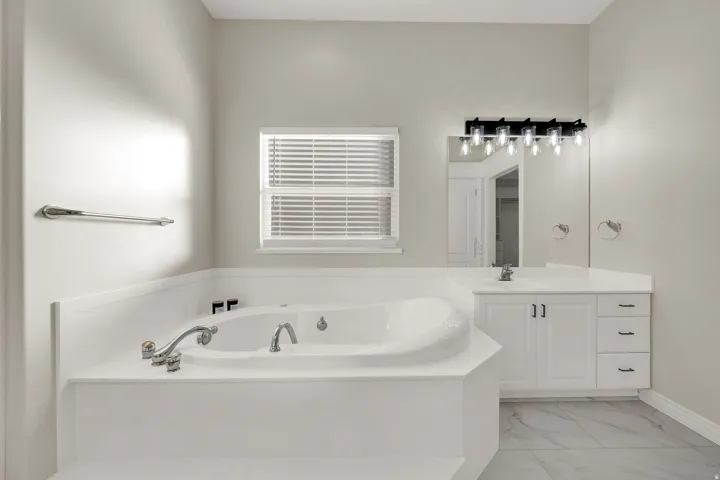 Built-in soaking tub with chrome fixtures, white vanity with integrated sink, quartz-finish countertop, and black vanity lighting