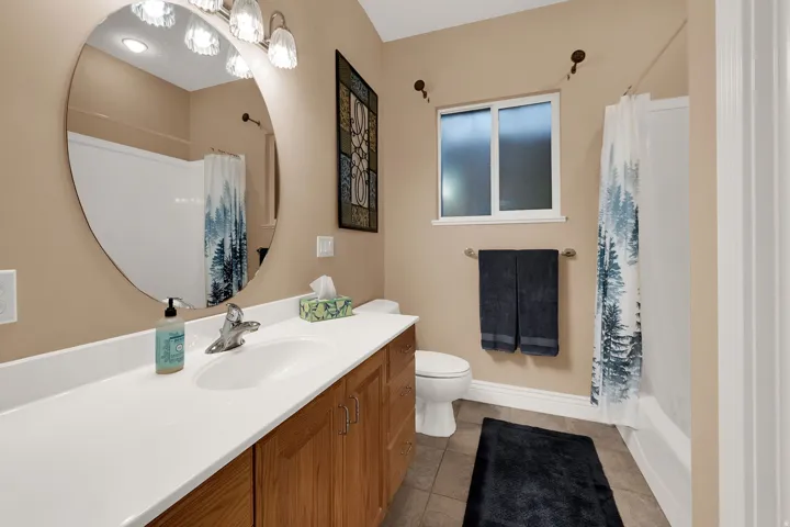 Bathroom featuring a spacious vanity with integrated sink, wood-finish cabinetry, and a large oval mirror