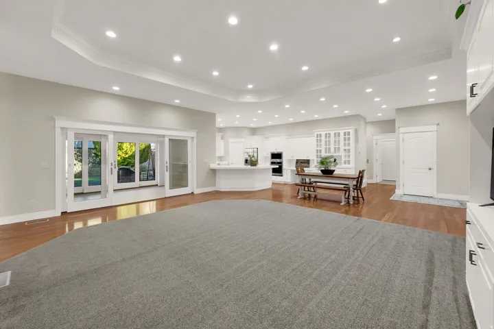 Recessed lighting illuminates an expansive room featuring a tray ceiling with crown molding, hardwood flooring, and sliding glass doors