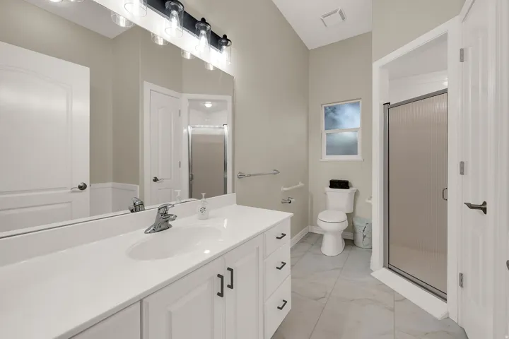 Spacious bathroom featuring a white vanity with integrated sink, large mirror, black and clear glass vanity lighting, tiled flooring, and a glass-enclosed shower