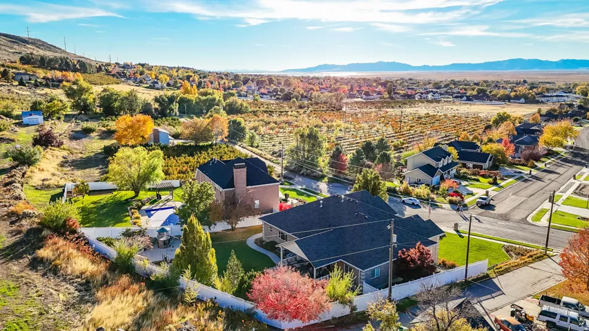 Aerial perspective showcasing a residential property with a dark shingle roof, a surrounding white fence, and mature trees