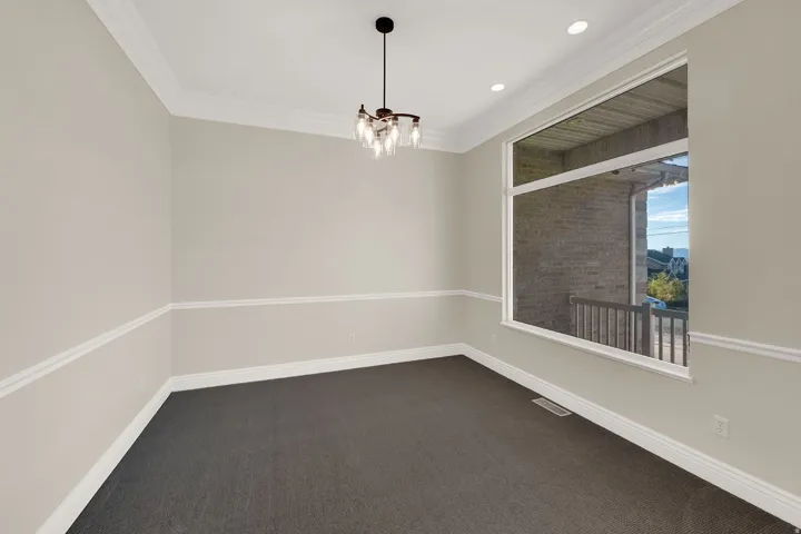 Formal room featuring crown molding, neutral wall tones with chair rail detailing, recessed lighting, and a modern chandelier
