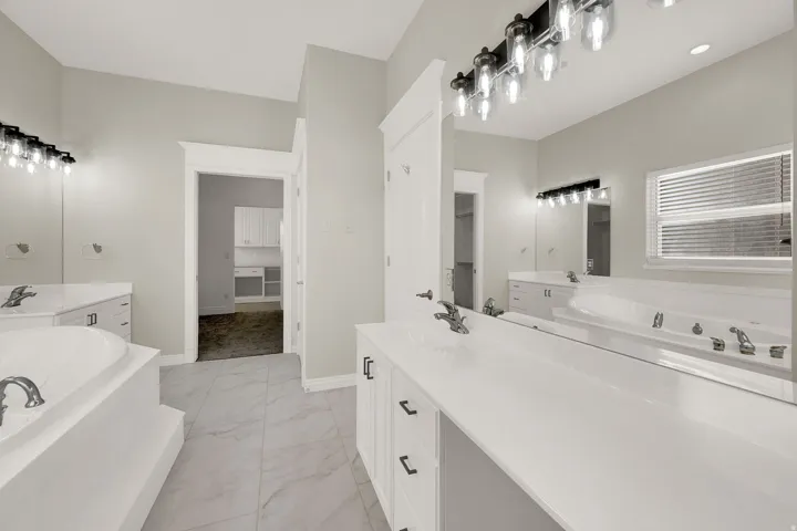 Spacious bathroom featuring a built-in soaking tub, dual vanity with white cabinetry, large vanity mirrors, and contemporary light fixtures