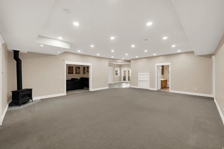 Expansive carpeted room featuring a freestanding black stove, recessed lighting, and multiple distinct entryways
