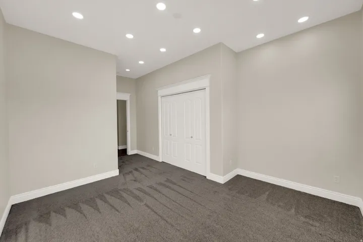 Spacious room featuring neutral-toned walls, recessed lighting, and dark grey carpeting