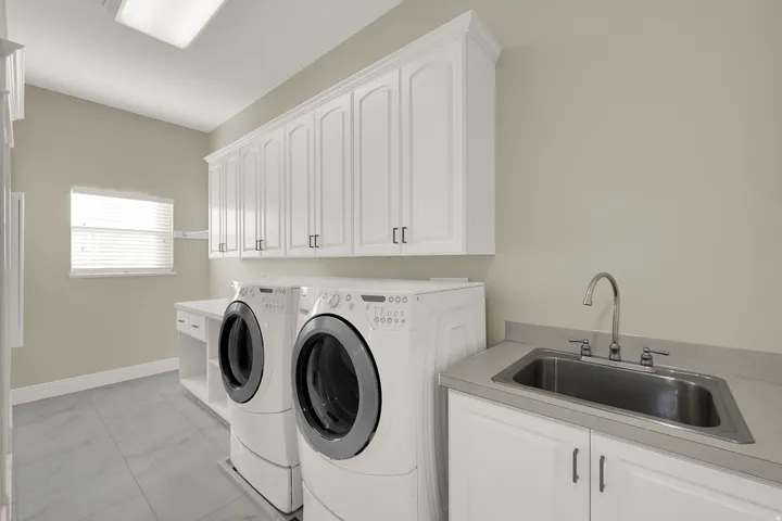 Dedicated laundry room featuring extensive white cabinetry, a built-in utility sink, a spacious countertop, and tile flooring
