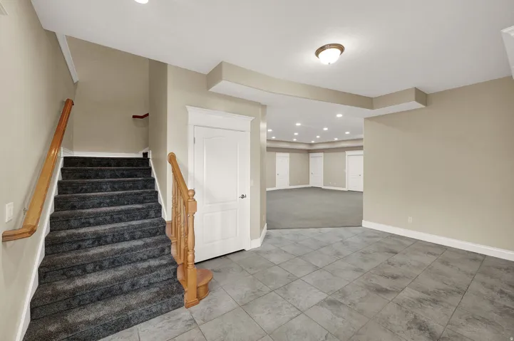 Carpeted staircase with wood handrails, opening to a tiled entry area