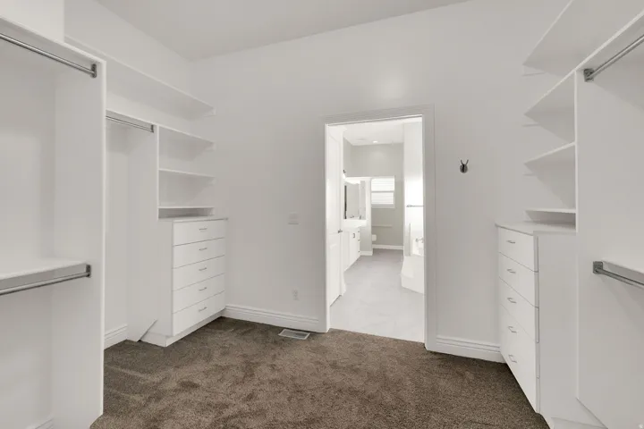 Walk-in closet with built-in white shelving, integrated drawers, and chrome hanging rods