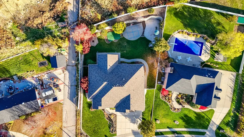 Expansive property featuring a multi-level roofline, extensive green lawn, concrete driveway, and a fenced swimming pool with surrounding patio