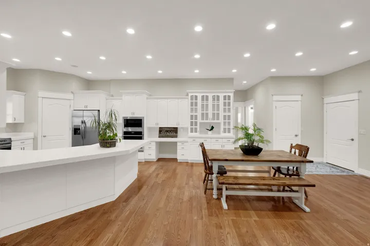 Open-concept kitchen and dining area featuring recessed lighting, extensive white cabinetry, built-in stainless steel appliances, a large kitchen island with a white countertop, and wood-finish flooring