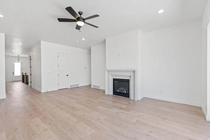 Spacious living area featuring light wood-finish flooring, a contemporary ceiling fan, and recessed lighting