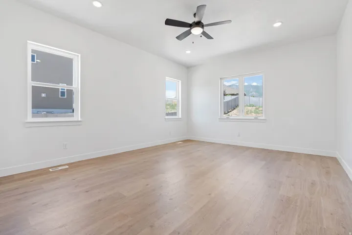 Spacious interior room featuring light wood-finish flooring, white walls, and a contemporary ceiling fan with integrated lighting
