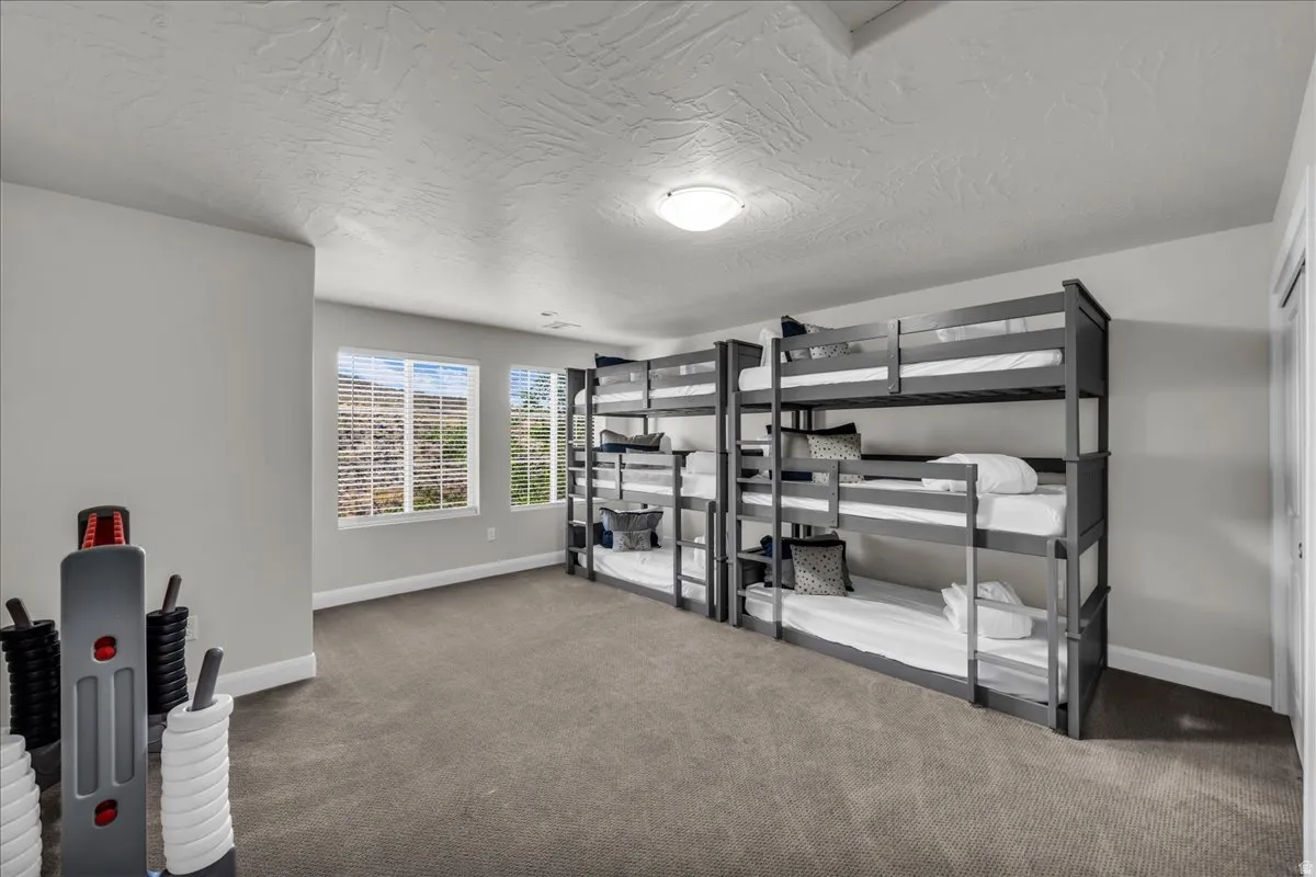 Spacious room with gray carpeting, two large windows with blinds, and white baseboards