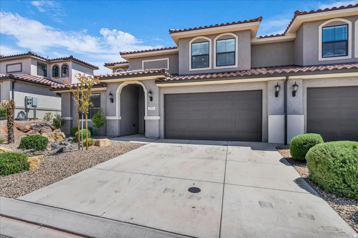 Contemporary stucco exterior featuring a terracotta tile roof, arched entry, two-car garage, and desert landscaping with decorative rocks and mature shrubs