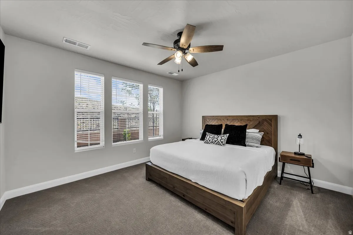 Carpeted room featuring three windows with blinds, a ceiling fan with light, and light-colored walls with white trim