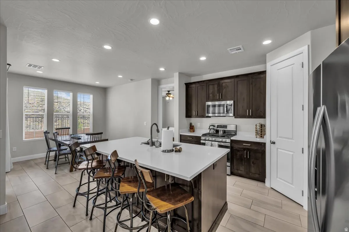 Open-concept kitchen featuring an oversized island with seating, dark wood cabinetry, white countertops, and stainless steel appliances