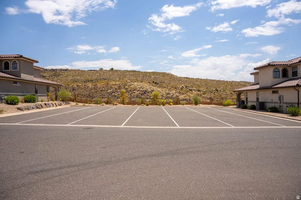 Paved parking lot featuring multiple marked spaces, surrounded by desert landscaping and stucco-finished buildings with arched windows and tile roofs