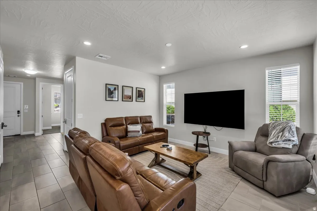 Spacious living area featuring light gray walls, recessed lighting, and multiple windows with blinds